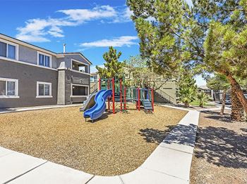 A playground with a slide and trees in front of a building